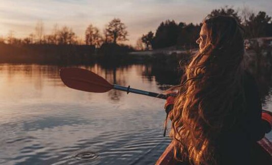 Persona remando en kayak por un río al atardecer
