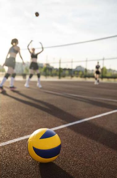 Balón de voleibol en primer plano y jugadoras junto a la red